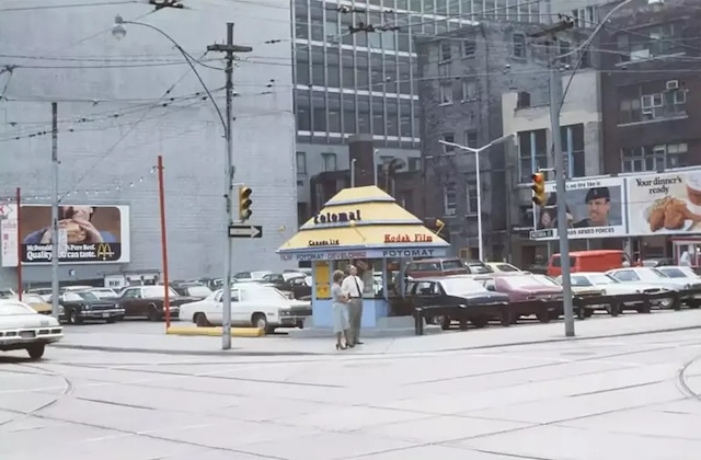 A city Fotomat booth on a busy corner, where drivers stopped to drop off or pick up their film