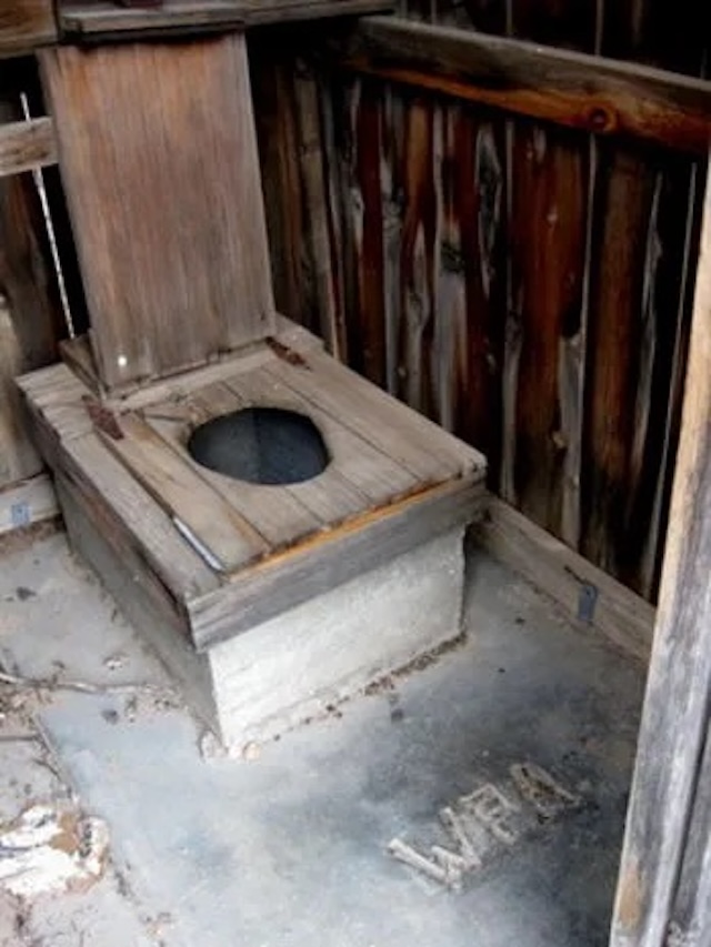 A traditional pit toilet made from wood and stone, showing the WPA (Works Progress Administration) mark, reminding us of historical infrastructure projects