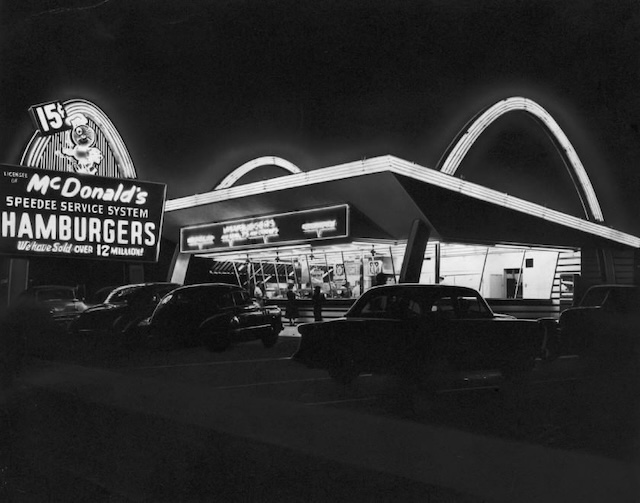 The original McDonald's restaurant at night, showcasing the Speedee Service System sign. The arches, now iconic, marked the dawn of fast food as we know it today