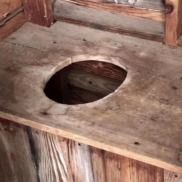 A close-up of the classic wooden pit toilet seat, a simple but essential structure used in outdoor sanitation systems of the past