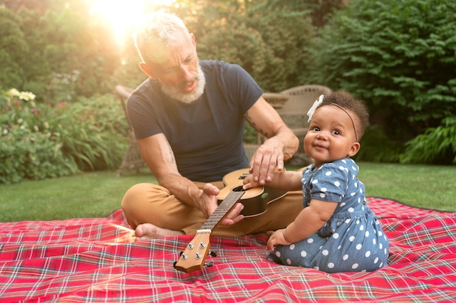 A grandfather bonds with his granddaughter, teaching her to play the ukulele under the soft glow of the afternoon sun