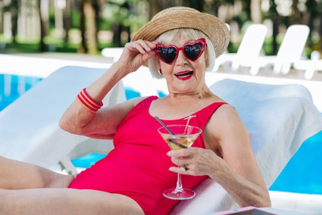 Red, stylish, and confident — this woman is living her best life, enjoying her day by the pool with a martini in hand and heart-shaped sunglasses on