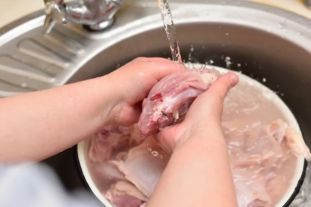 A close-up of rinsing chicken in the sink—a controversial practice that experts often discourage