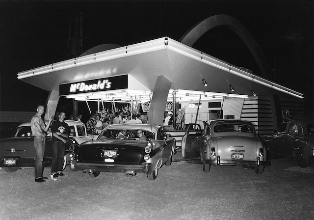 Teens gather at a McDonald's drive-in, enjoying burgers and fries under the glow of the famous golden arches, capturing the spirit of 1950s American youth culture