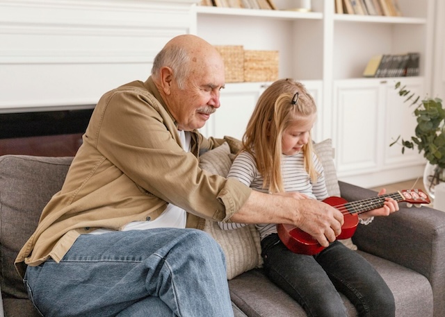 A grandfather patiently shows his granddaughter how to play the ukulele, sharing his love for music across generations