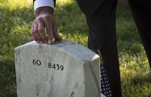 A man gently places coins on a grave, continuing the tradition of honoring a loved one or comrade who has passed