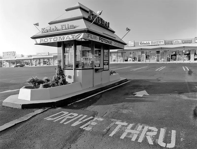 A black-and-white view of a Kodak Fotomat booth with "Drive-Thru" marking, reminding us of a quick yet non-instant era of photo developing