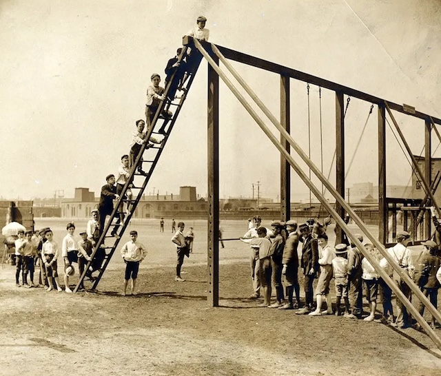 Children queue eagerly to climb a tall, narrow slide, with no soft landing in sight. Playgrounds like this highlight the boldness of past generations