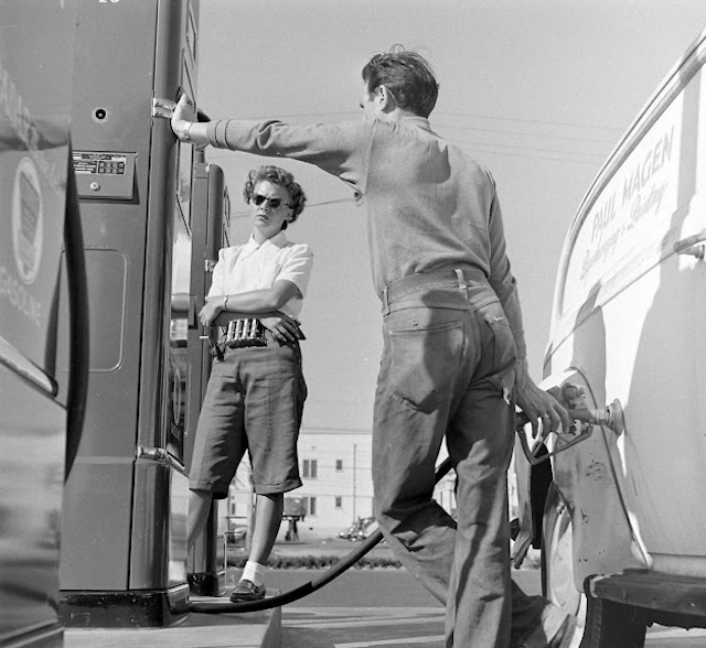 A customer refuels their car under the watchful eye of an attendant, a scene emblematic of the personalized service typical at American gas stations in the mid-20th century