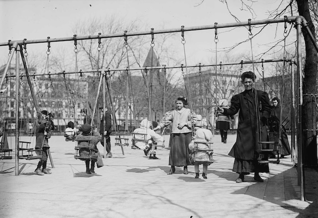 Parents and children enjoy a communal outing at the local playground. The lack of modern safety standards contrasts sharply with the carefully engineered play spaces of today