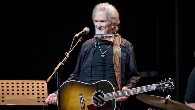 Kris Kristofferson performing live, harmonica in hand, radiating the charisma and passion that kept him on stage well into his later years