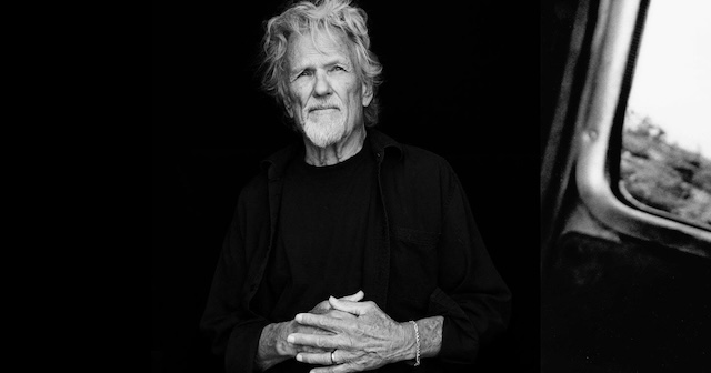  Kris Kristofferson standing strong in black and white, his posture and expression embodying the gravitas and humility that defined his long career