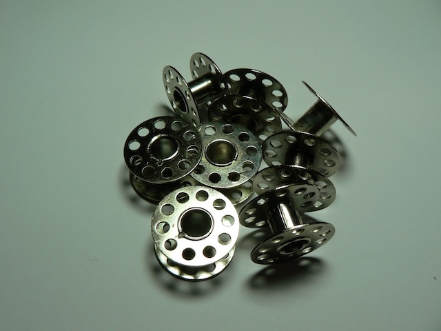 A pile of vintage sewing machine bobbins, their metal gleaming, symbolizing the hard work and craftsmanship they enabled in homes and factories