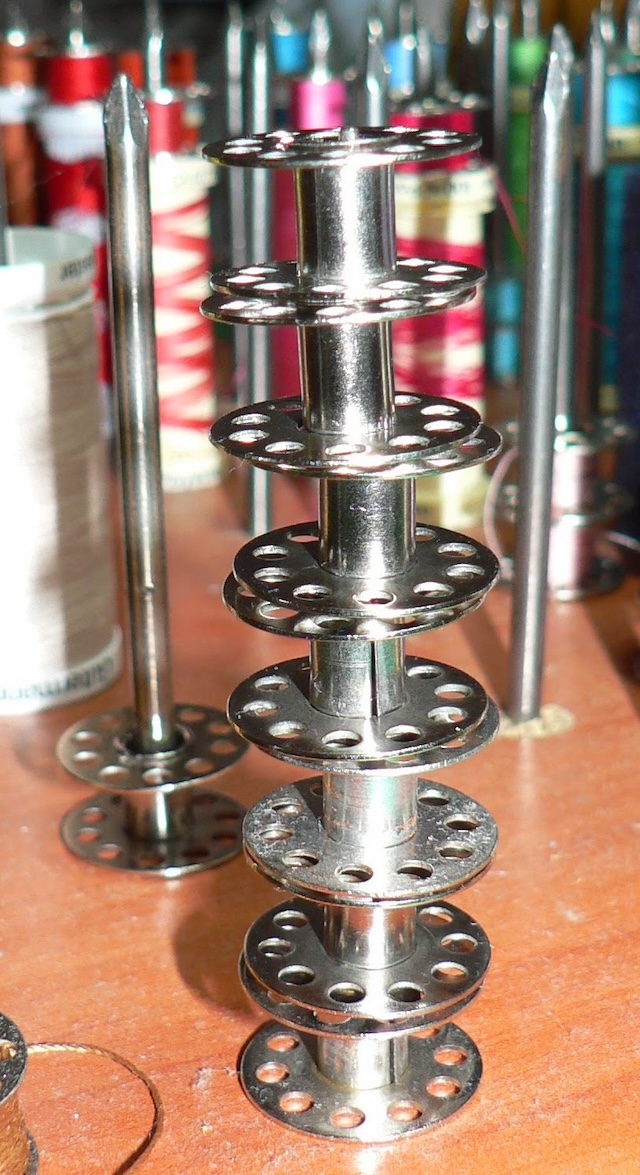 A playful stack of vintage sewing machine bobbins standing tall among colorful spools of thread, representing the essential role they played in sewing projects