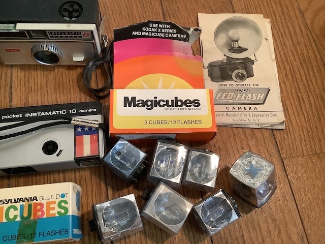 A nostalgic collection of vintage photography equipment, including Sylvania Flash Cubes, vintage cameras, and classic camera manuals from the golden era of instant photography