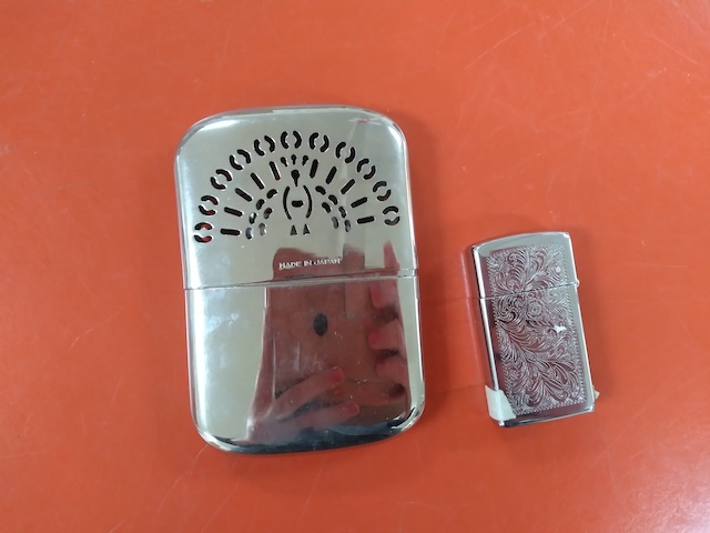 A larger vintage hand warmer, next to a standard lighter for size comparison