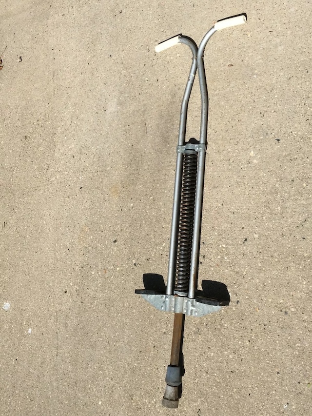 A complete view of the vintage pogo stick, standing tall on a concrete surface. The wear and tear of time are visible, but it still looks ready for a fun jump or two