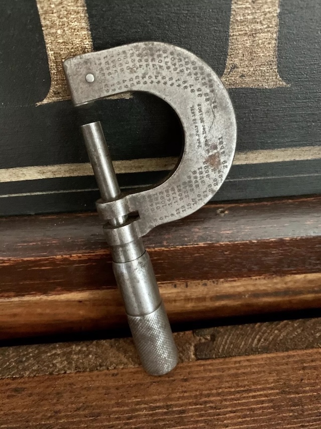 An antique micrometer resting on a wooden workbench, possibly used in precision engineering or metalworking for decades