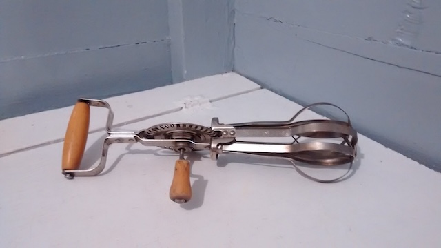 A side view of the vintage hand-crank egg beater with its wooden handle, a nostalgic reminder of simpler times in baking and cooking