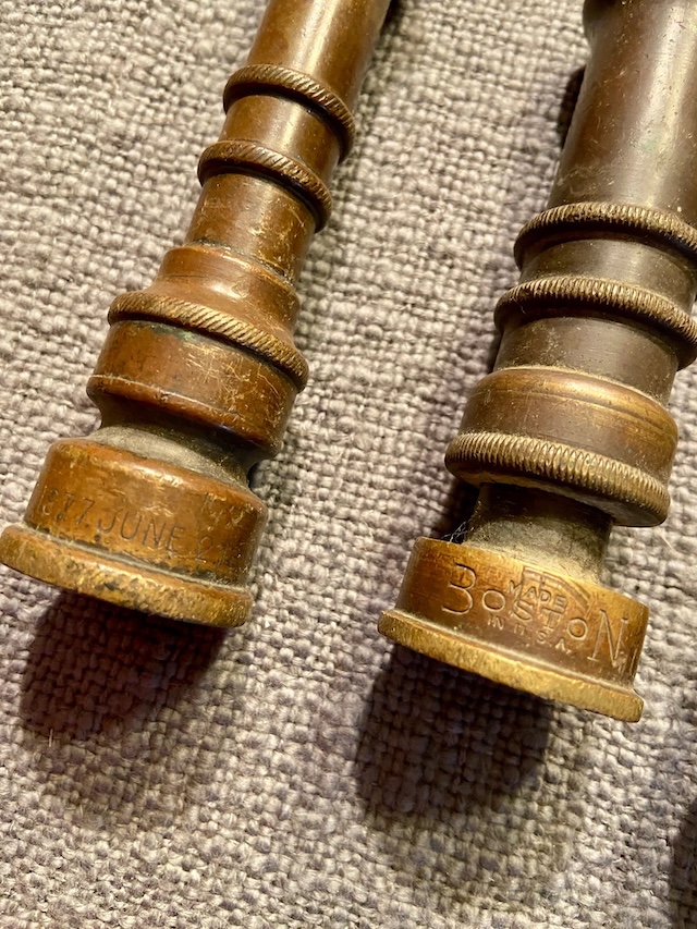 Close-up details of the intricate engravings on two vintage GEM brass water nozzles, dated and stamped with "Boston" to mark their origins