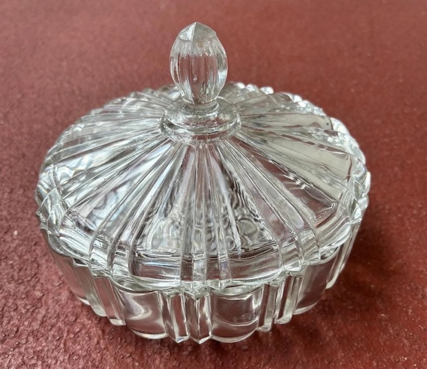 The glass candy dish in all its nostalgic beauty, resting on a retro red surface. Just lifting that lid could make the entire room know you were sneaking a treat