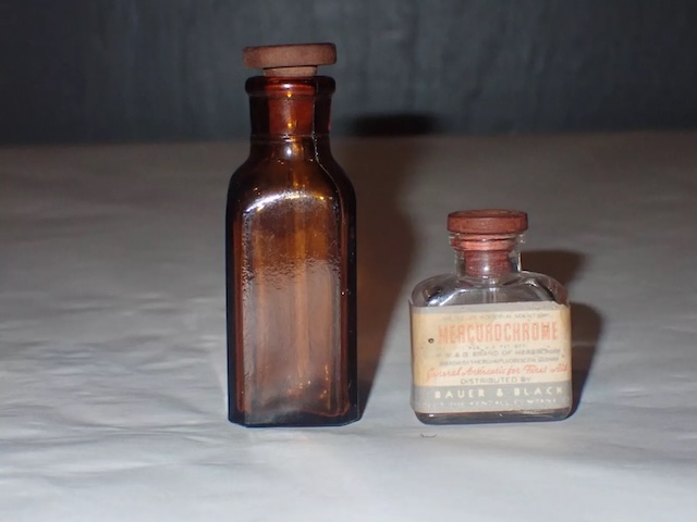 Two antique bottles of Mercurochrome, one featuring the well-known label distributed by Bauer & Black, reflecting the history of the product’s widespread use across various manufacturers