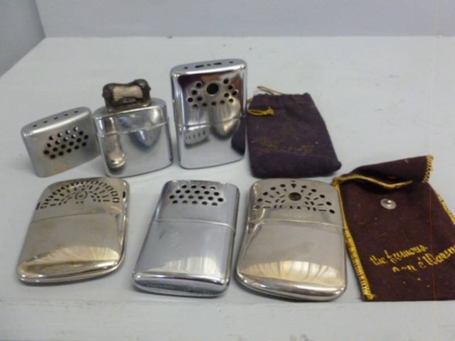 A variety of vintage hand warmers from different decades, each with its own unique style and original cloth bags