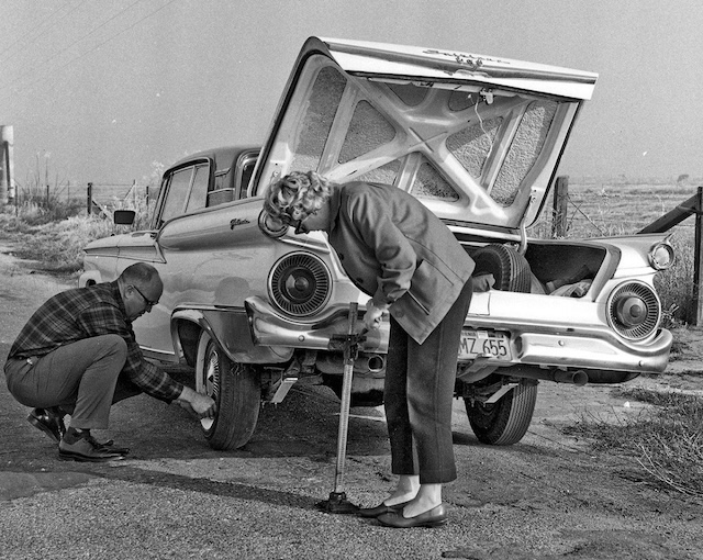 A couple working together to fix a flat tire—vintage bumper jack in action. A true flashback!