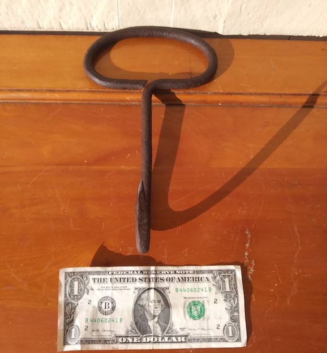 Comparing size to a dollar bill, this photo highlights how compact the antique hay hook is, yet how powerful it was in the hands of those who worked with hay daily