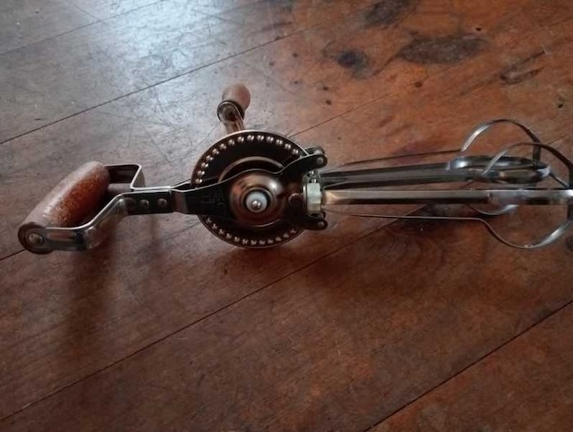 A well-preserved vintage hand-crank egg beater resting on a wooden surface, still functional after years of use, a testament to its durable design