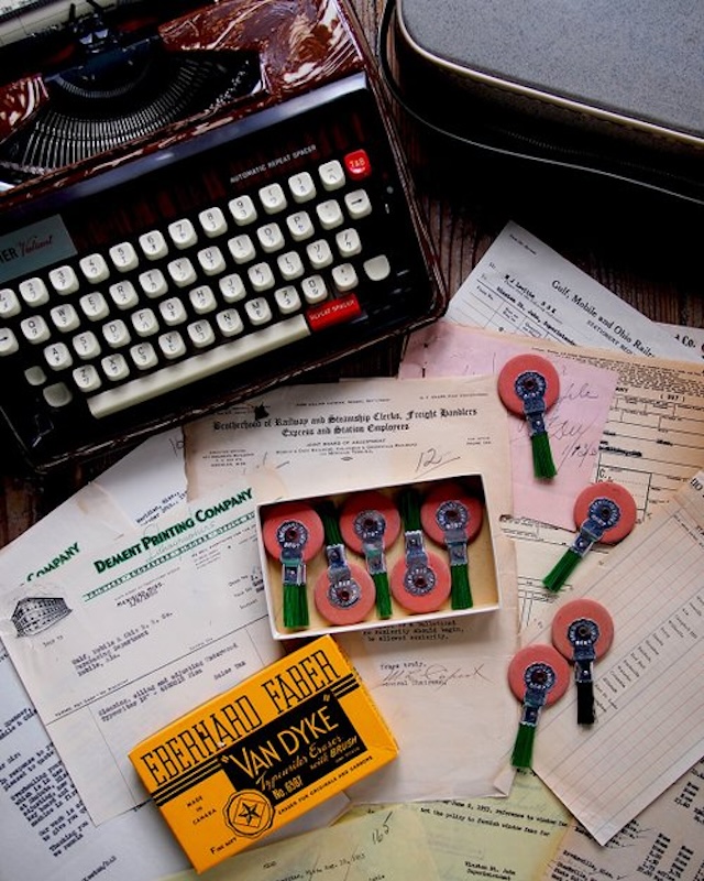 A vintage office desk complete with a typewriter, vintage erasers, and paperwork. This setup will bring back nostalgia for many who remember when every word was typed by hand