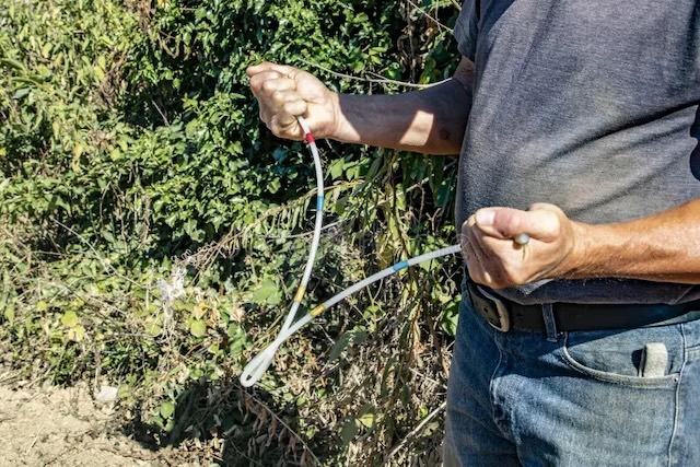 Holding a bent rod, this dowser stands poised, continuing a practice that blends tradition, belief, and skill in locating water sources