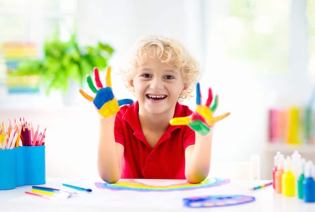 A child beams with pride as their colorful hands reveal their vibrant imagination