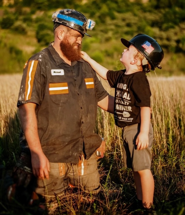 Michael and his son Easton connect over a shared moment in the open fields, dressed in their miner gear, symbolizing the hard work that supports a loving family