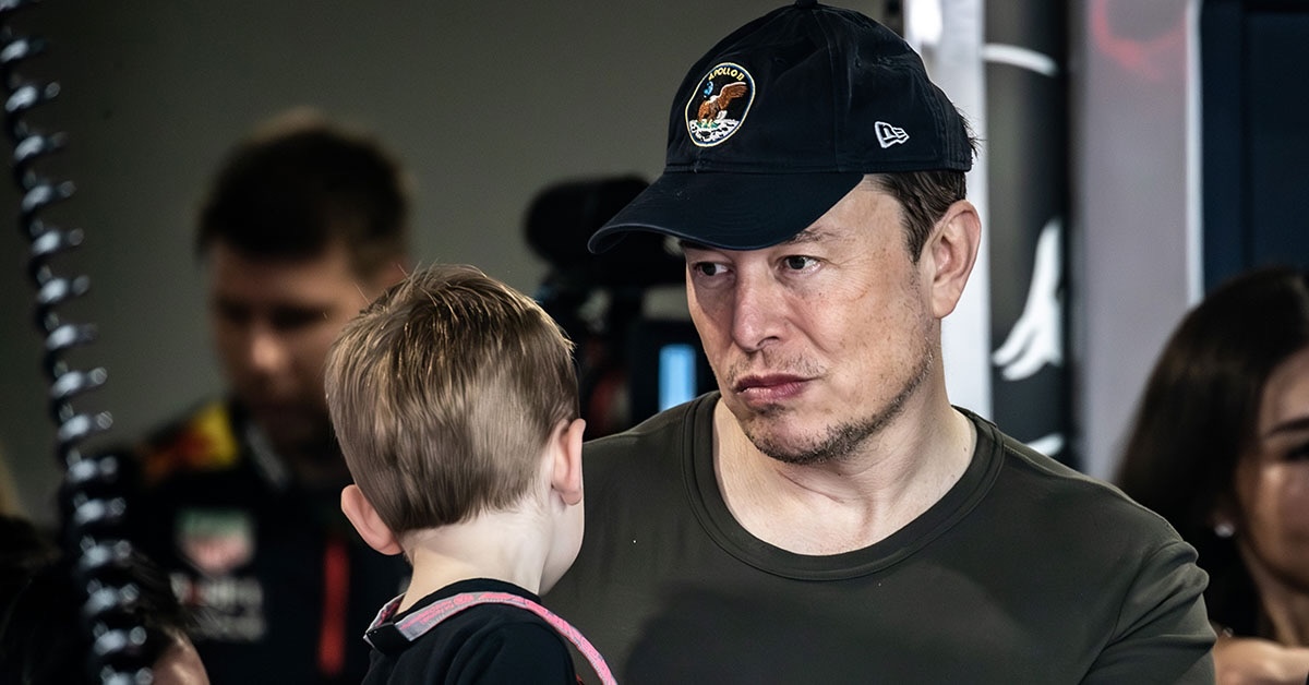 Elon Musk with one of his sons, looking focused while taking in the event around them