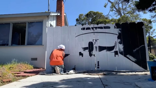 Etienne working meticulously on the mural, transforming the fence into a statement piece that merges art with compliance