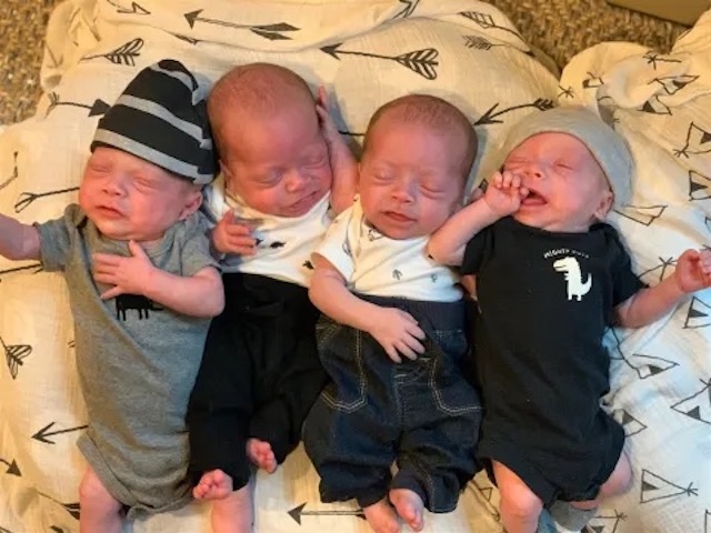 Four adorable babies, each dressed in different onesies, resting peacefully together for the first time at home