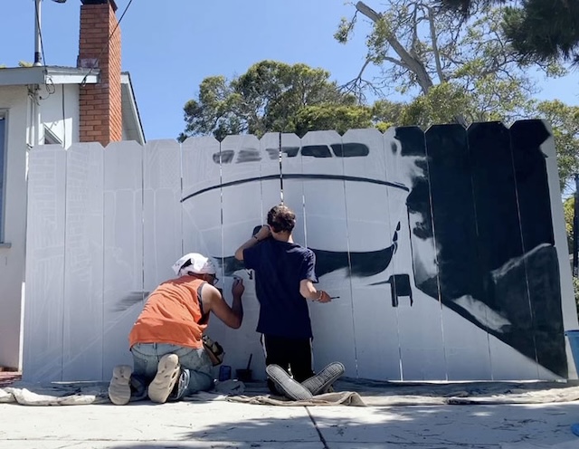 Etienne and a collaborator adding finishing touches to the mural, highlighting the collaborative effort behind the masterpiece