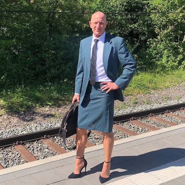 A sharp formal look with a teal suit, skirt, and stiletto heels, standing confidently by the railway tracks