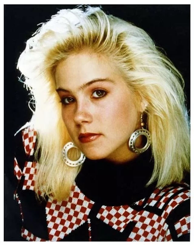 Christina Applegate in her iconic early 80s look, with dramatic hair and statement earrings that became part of her signature style