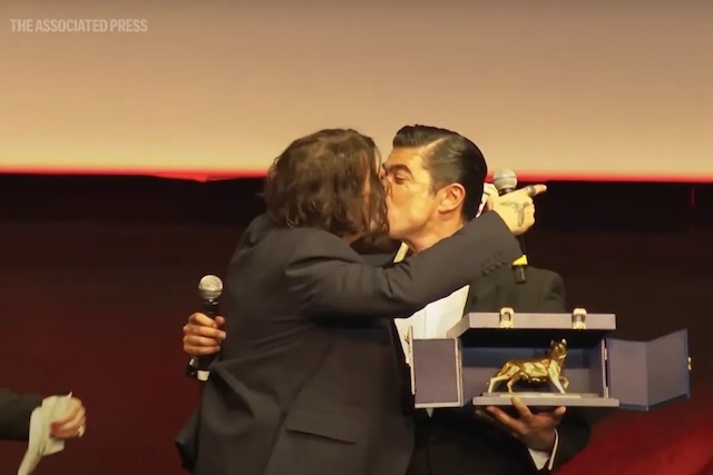 A light-hearted moment unfolds on stage as Depp shares a friendly peck with Riccardo Scamarcio, prompting cheers and laughter from the audience