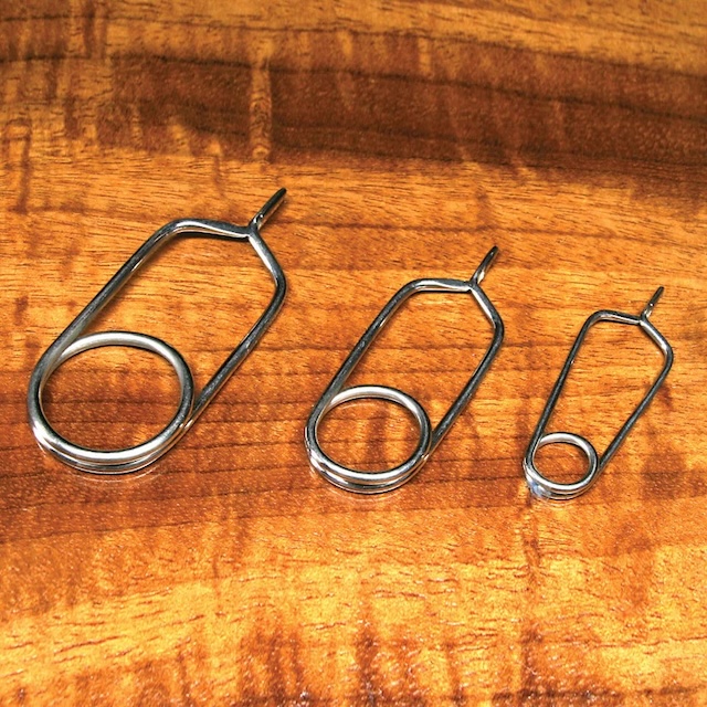 Three sizes of hackle pliers on a wooden table—perfect for handling different feather widths in the art of fly tying