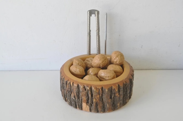 The rustic finish of the tree bark bowl beautifully complements the shiny metal nutcrackers, adding a touch of nature to your kitchen décor