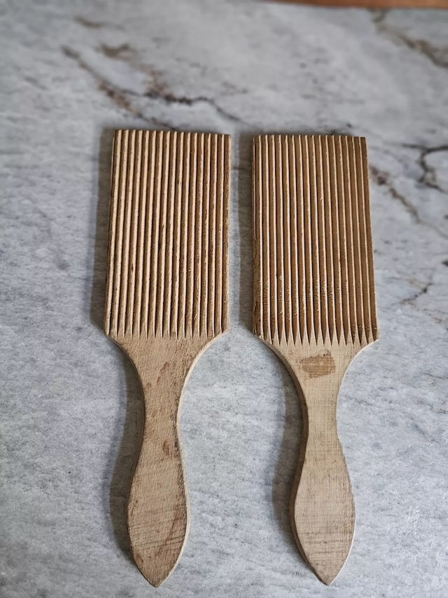 Close-up of the grooved butter paddles against a marbled surface, capturing the wear and patina of years of use. The grooves ensured butter was shaped evenly and efficiently