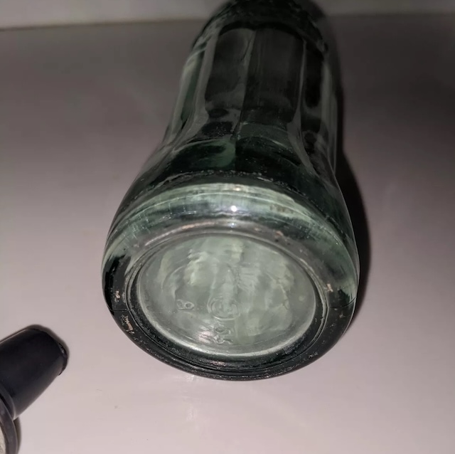 A close-up of the base of the vintage glass sprinkler bottle, revealing its smooth glass bottom and subtle vintage wear