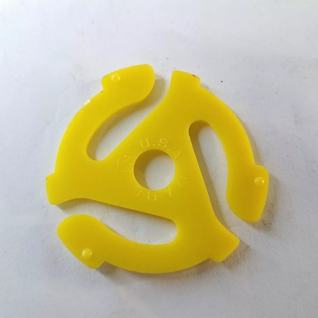 A close-up of a yellow 45 RPM record adapter, featuring clear embossing that hints at its manufacturing origin