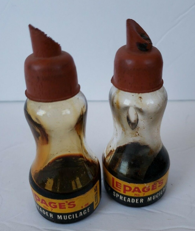 A pair of well-used Lepage's Mucilage Glue bottles, with their signature curvy shape and aged spout tops, reflecting their history in many homes