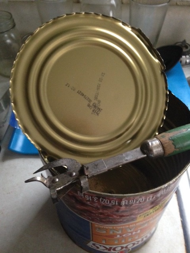 A side perspective of the can opener, featuring its vibrant red wooden handle with charming signs of wear from decades of use