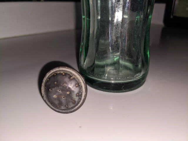 A detailed view of the metal cap removed from the vintage sprinkler bottle, highlighting the perforations used to sprinkle water evenly