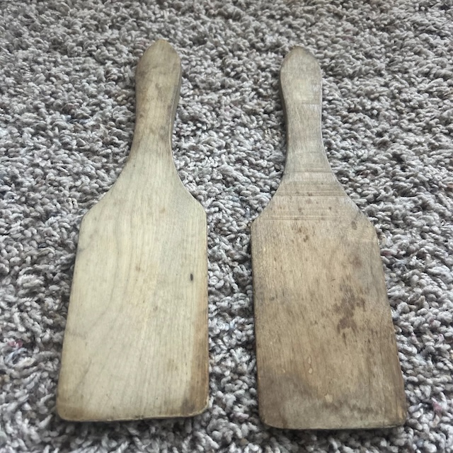 A weathered set of butter paddles lying on a carpeted surface, showcasing their well-used condition. They evoke memories of homemade dairy products and hand-crafted care